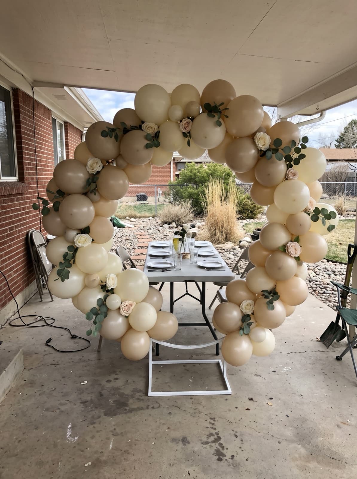 Floral balloon arch with eucalyptus over a brunch table on a covered patio