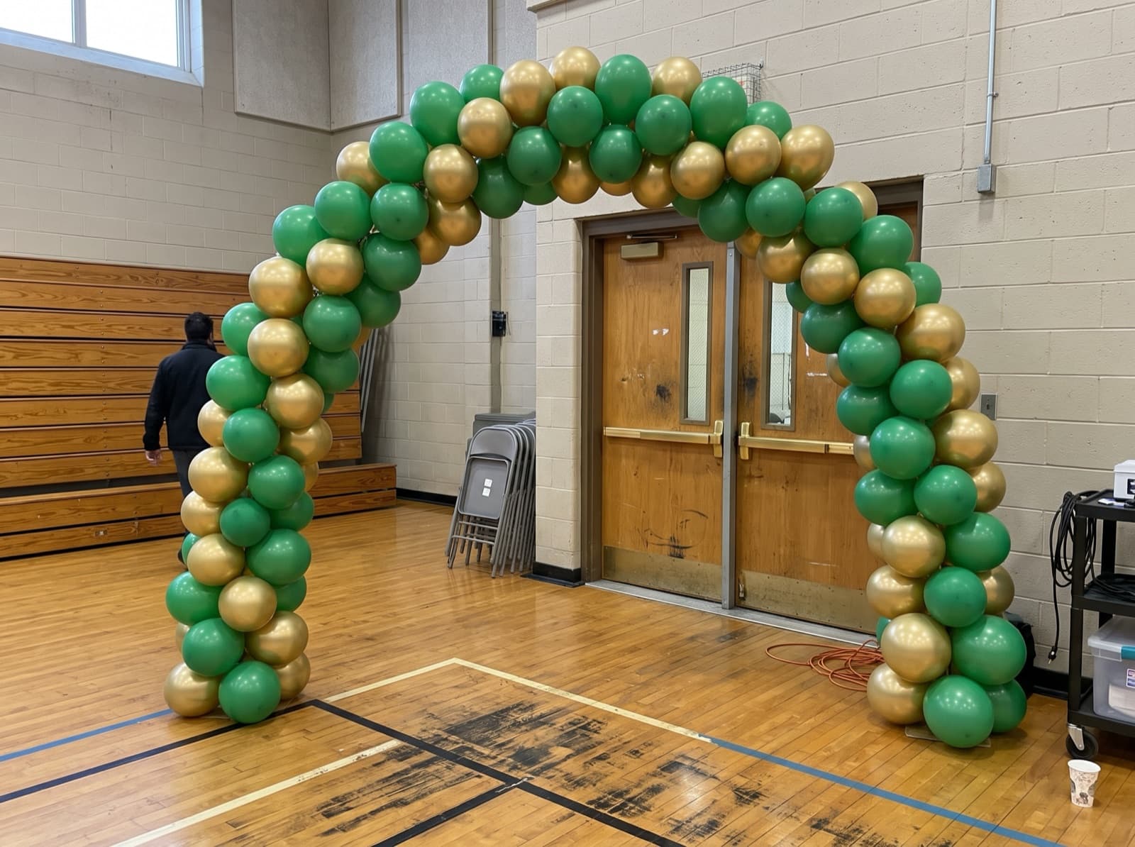 Spiral balloon arch in green and gold over a school gym entrance